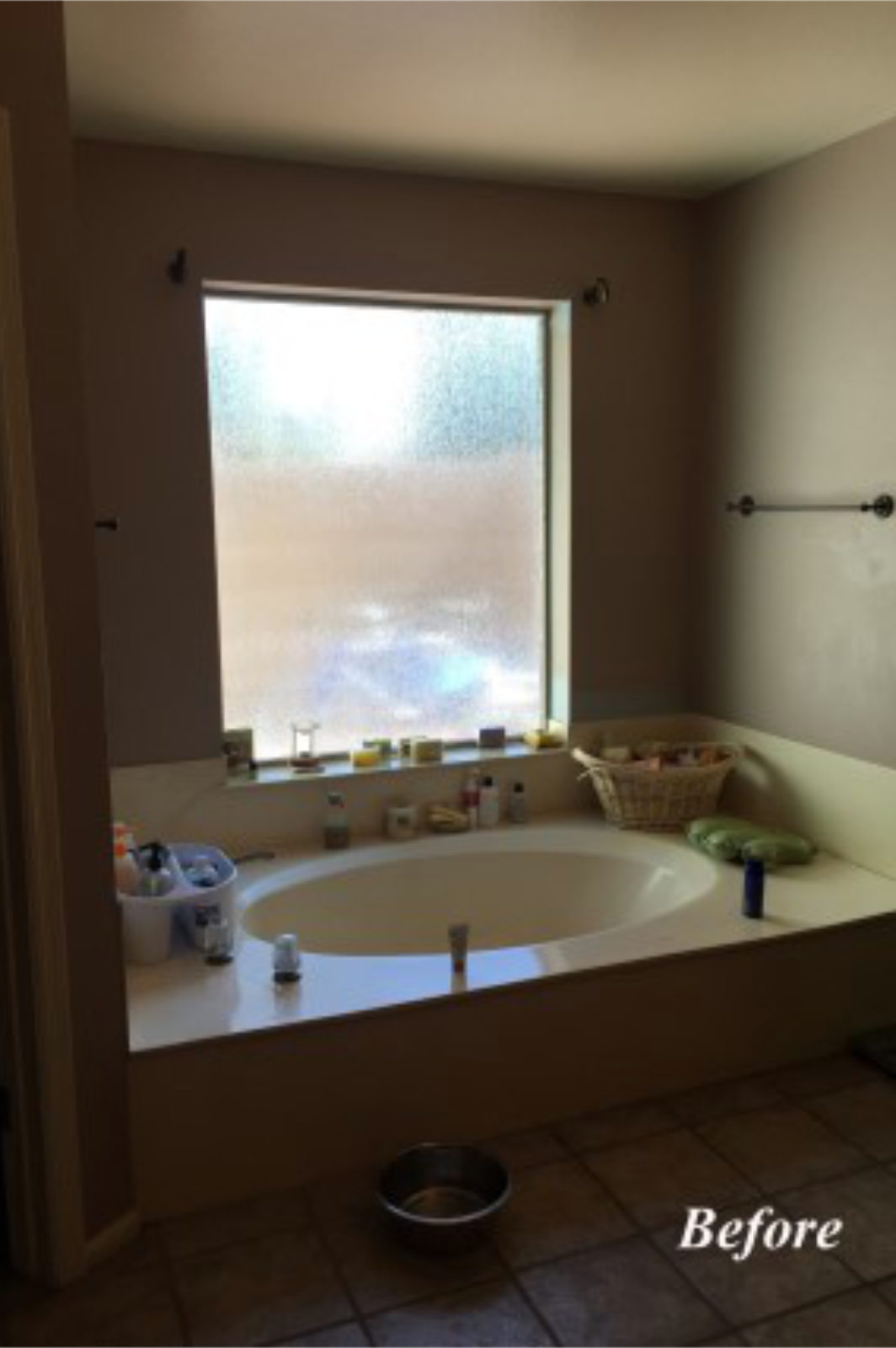 Original tub area at the Tempe bathroom with a cultured marble bathtub set in a wide tile deck, beige walls, and personal products cluttering the deck.