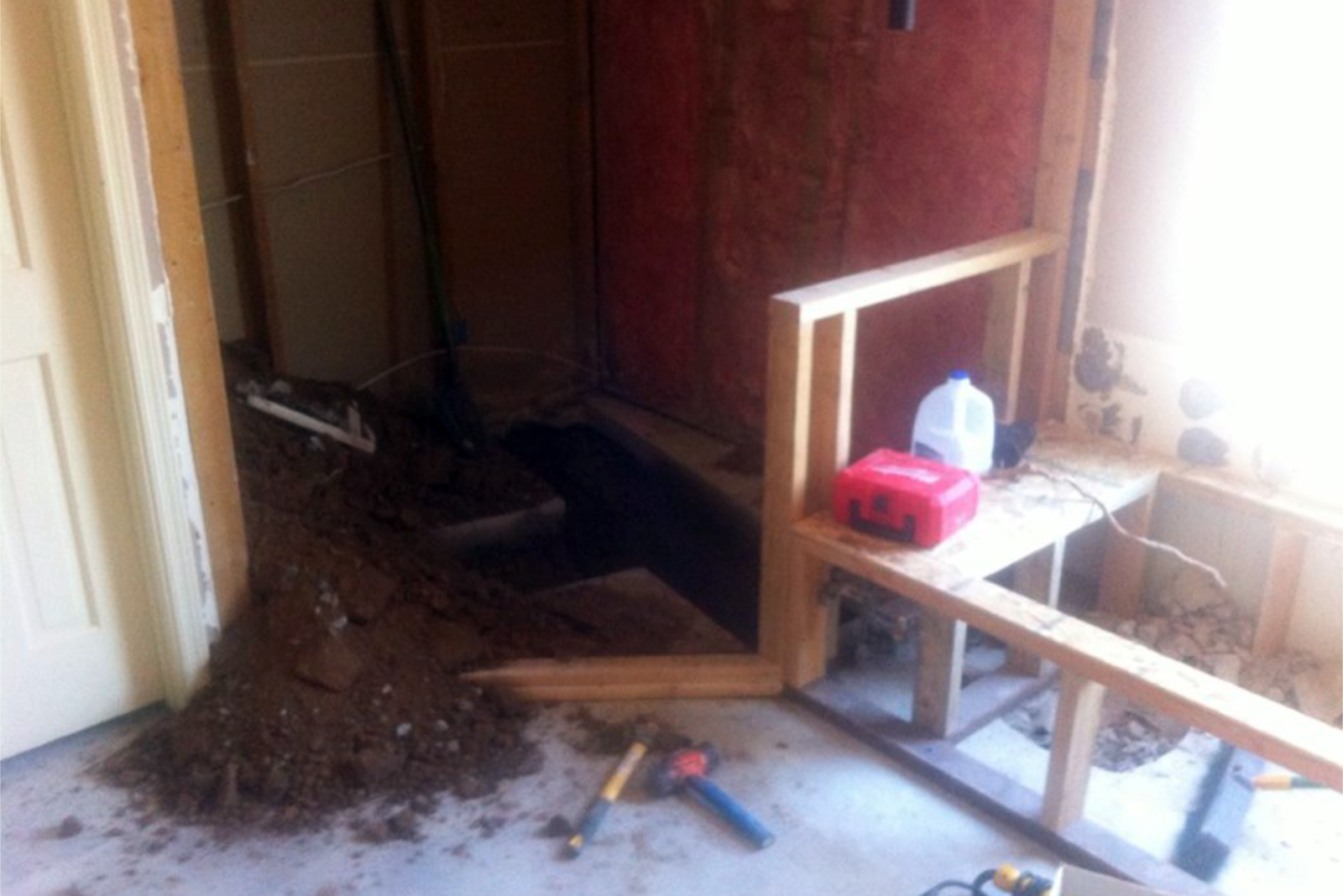 Concrete slab cut at the Tempe bathroom remodel during plumbing relocation for the new shower drain, with framing for the new walls underway.