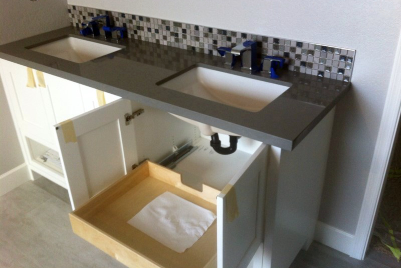 Custom vanity installation at the Tempe bathroom remodel with quartz top, undermount Kohler sinks, mosaic tile backsplash, and a pull-out drawer open under one of the sinks showing the wood storage interior.