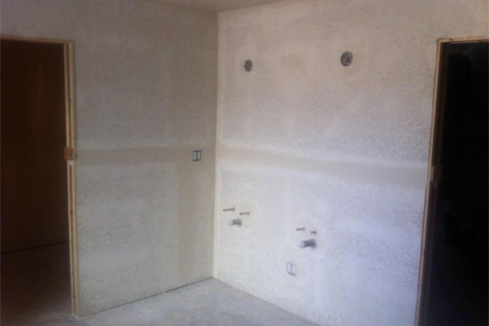 Drywall patched and ready for primer at the Tempe bathroom remodel, showing the new shower wall with two showerhead rough-ins and the pocket door cavity framed on the left.