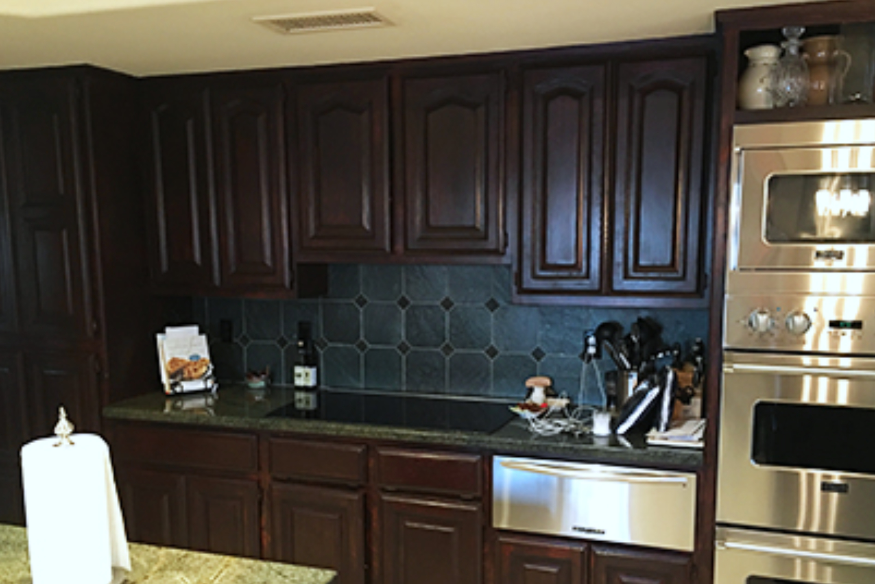 Original cooktop wall in the Phoenix kitchen with dark wood cabinets, blue diamond pattern tile backsplash, and stainless wall ovens.