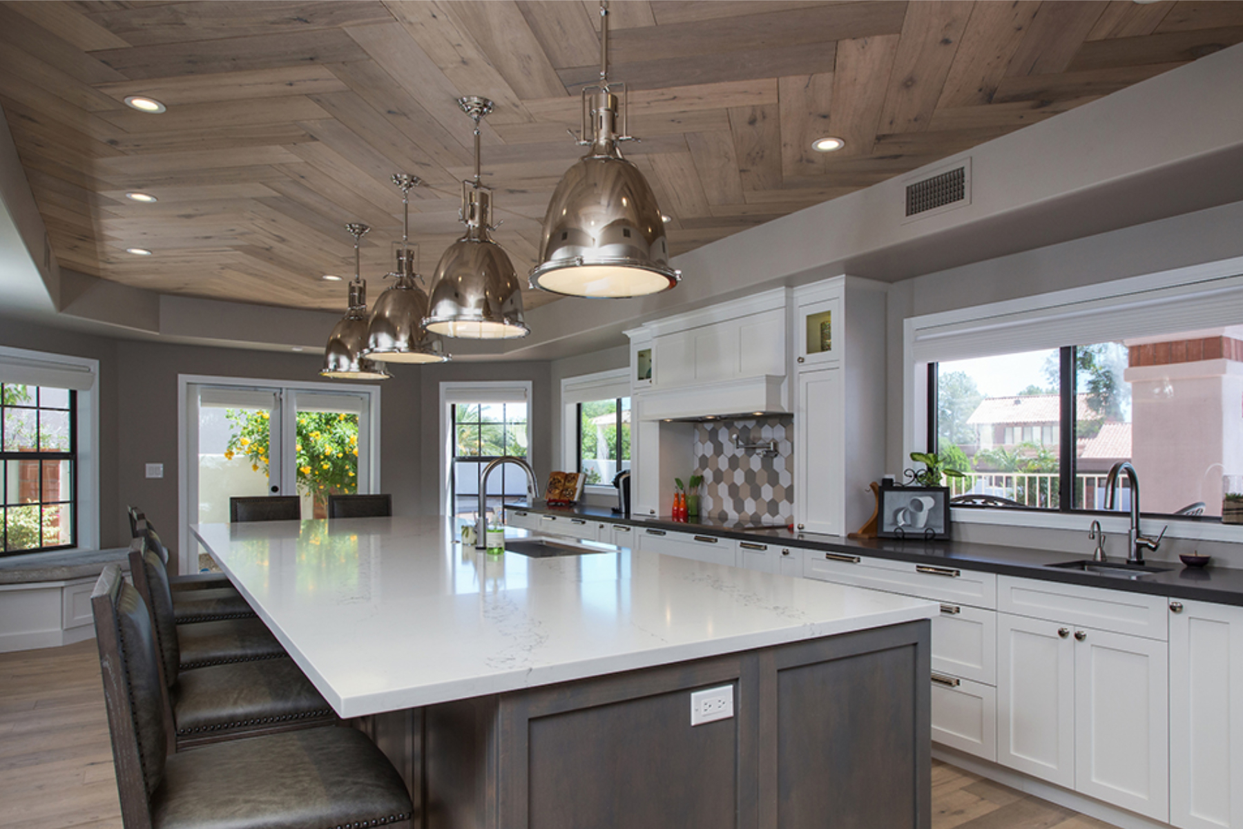 Open great room view at the Phoenix kitchen after wall removal, showing the new island, white cabinets, wood ceiling, and pendant lights.