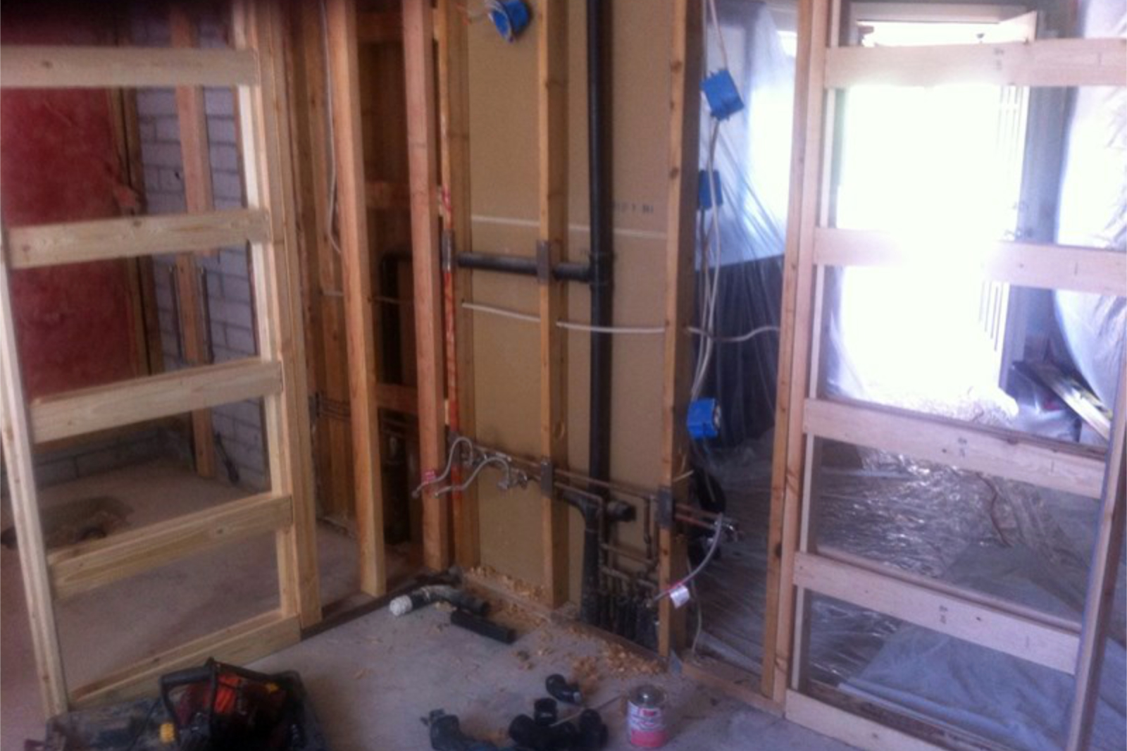 Framing and rerouted plumbing at the Tempe bathroom remodel, with the new pocket door cavity on the left and the relocated drain and supply lines visible in the center wall.