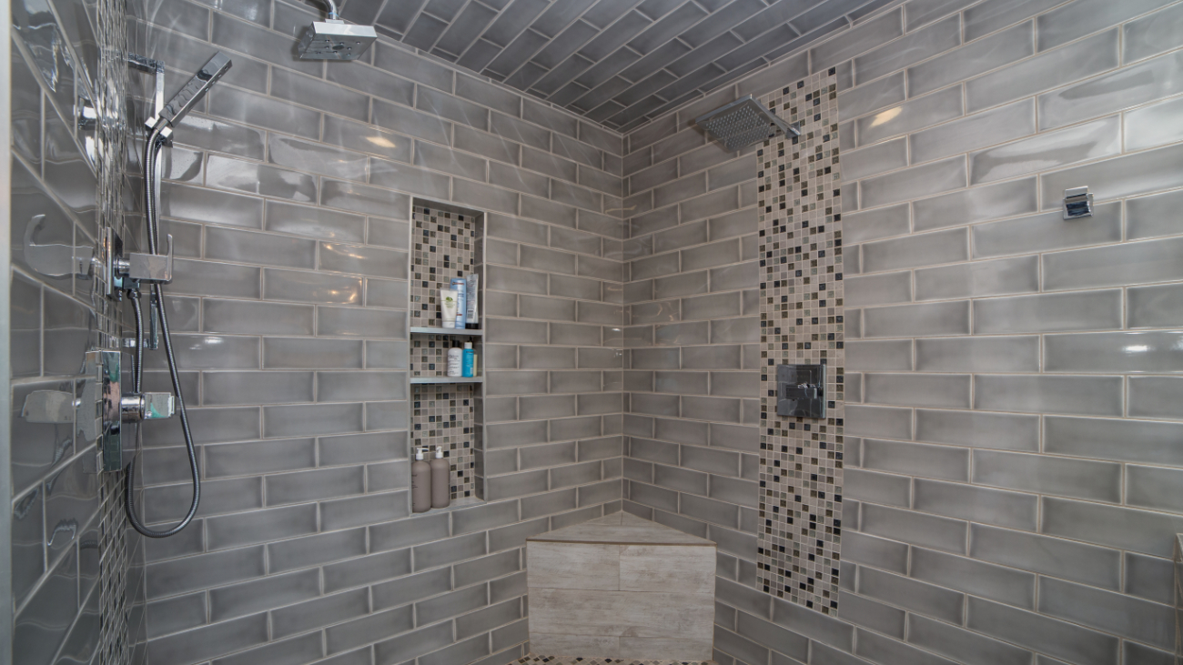 Inside the walk-in shower at the Tempe bathroom remodel, with two showerheads, recessed niche framed by Kismet Fate mosaic accent, vertical mosaic accent band, tile bench running the full back wall, and mosaic tile floor.