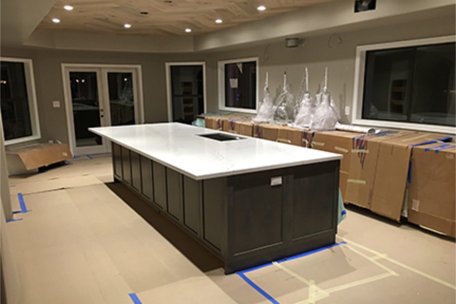 Cabinets and quartz countertops installed at the Phoenix wood-ceiling kitchen, with ramboard floor protection and cardboard wrapping protecting the new cabinets during the remaining trade work.